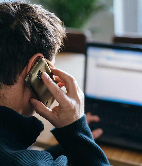 Man on cell phone looking away at computer screen