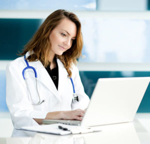 Female healthcare worker standing at desk looking at laptop