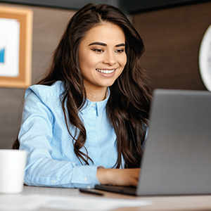Woman smiling looking at laptop with coffee mug