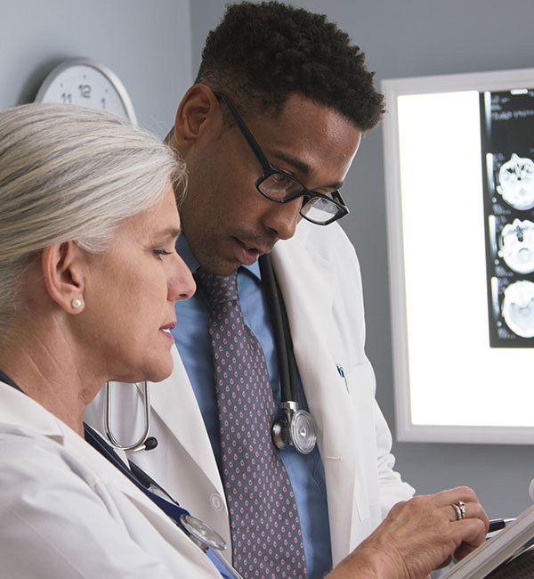 Female doctor showing report to male doctor with MRI in background
