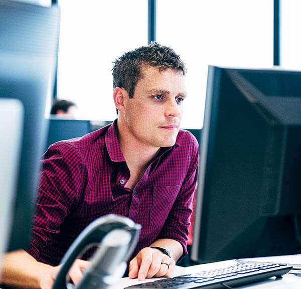 Adult male in red and blue shirt looking at computer monitor in an office