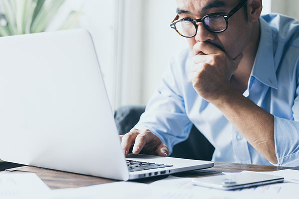 Man with glasses on right looking at laptop intently