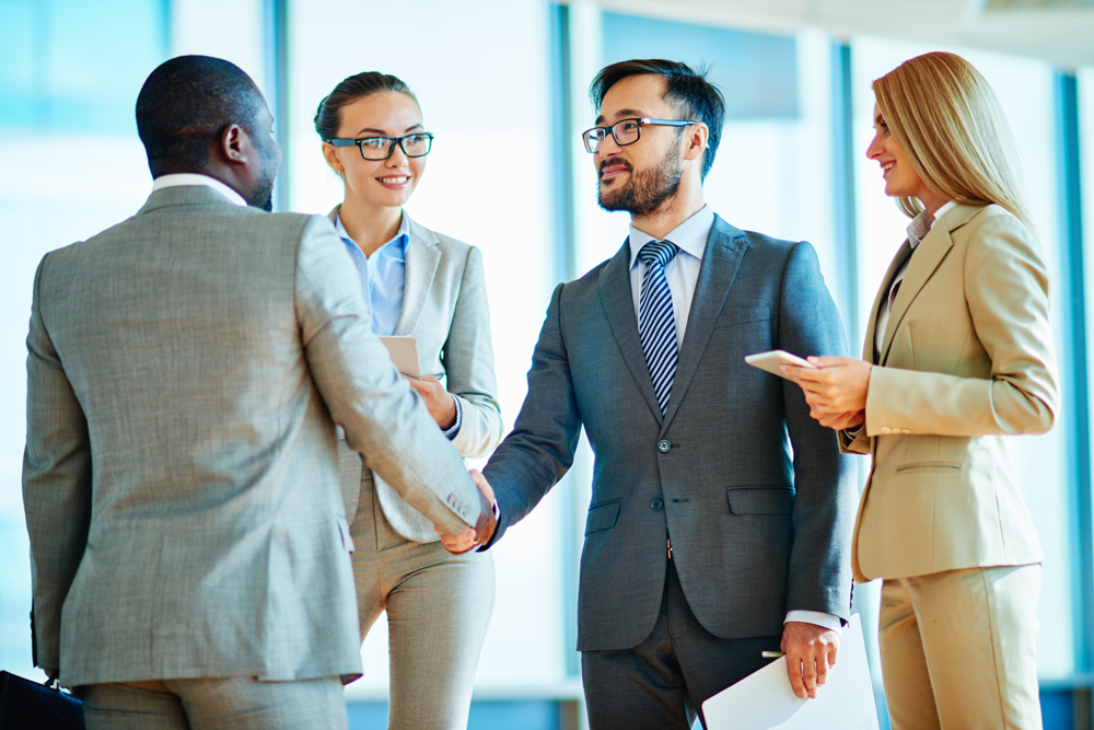 Two men in business suits shaking hands and two women in business suits watching