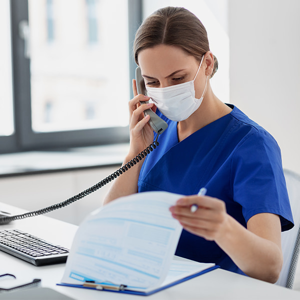 Female nurse wearing a mask looking at paperwork while on the phone