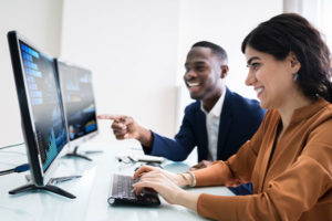 Male and female coworkers looking at two screens of data