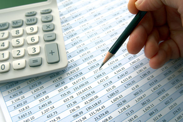 Hand with a pencil pointing as paperwork with large table of numbers